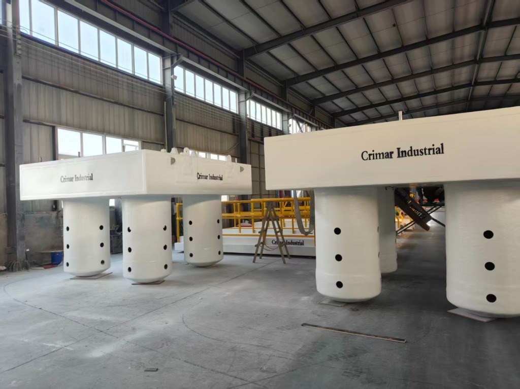 Two white FRP pump barge hulls standing on ported ballast columns in the fabrication shop