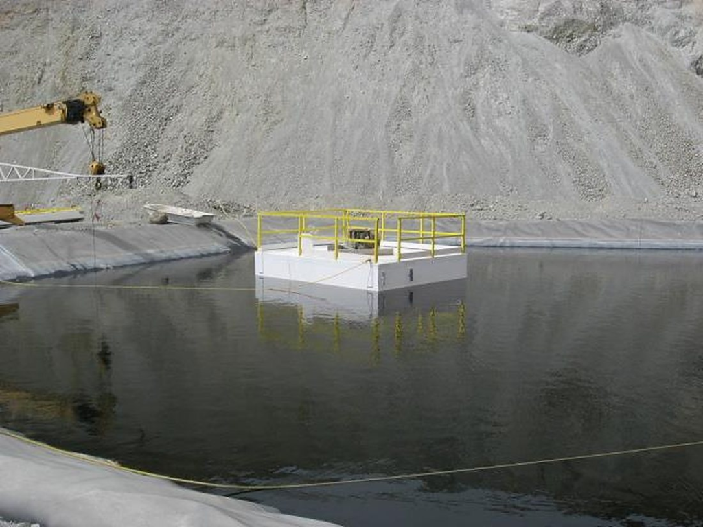 White FRP pump barge with yellow fiberglass handrail floating in an HDPE-lined mine pond