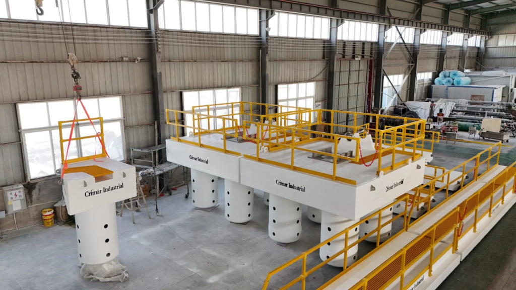 FRP pump barges fitted with yellow handrail beside a floating walkway, with a ballast column lifted on the shop crane